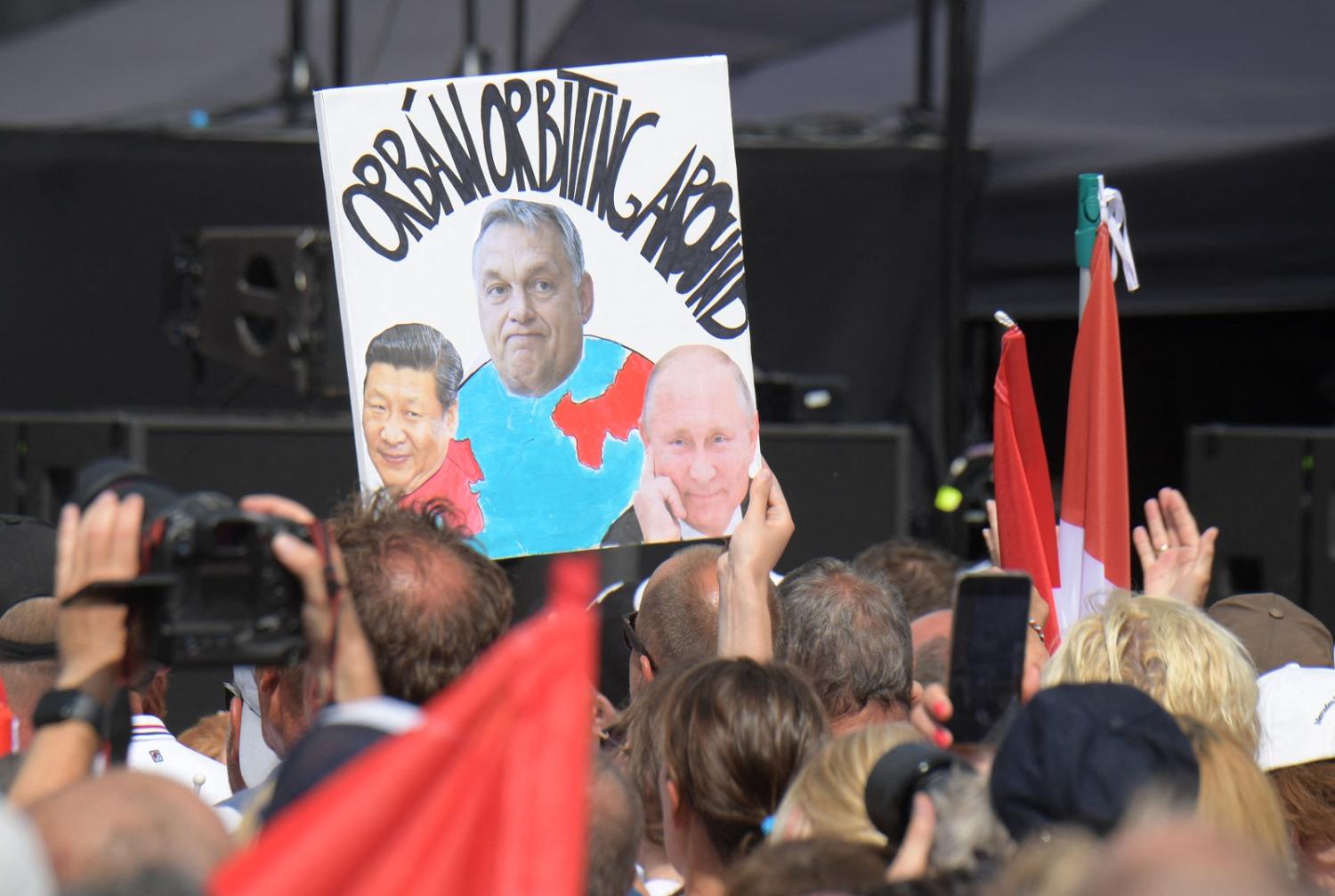 A protestor holds a poster depicting Russia's President Vladimir Putin and China's President Xi Jinping orbiting around Hungarian Prime Minister Viktor Orban during an anti-government rally on 8 June 2024 in Hungary (Ferenc Isza/AFP via Getty Images)