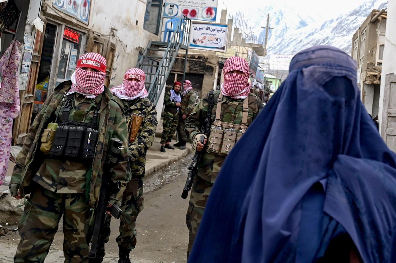 Taliban security personnel stand guard as an Afghan burqa-clad woman walks along a street in the Baharak district of Badakhshan province, 26 February 2024 (Wakil Kohsar/AFP via Getty Images)